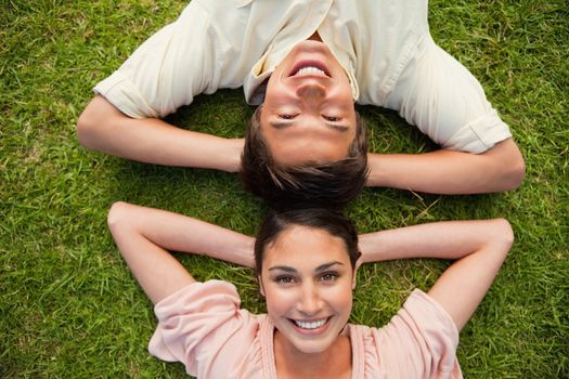 Man and a woman smiling while lying head to head with both of their arms resting behind their neck on the grass