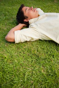Man lying down in grass with his eyes closed and both of his hands resting behind his head