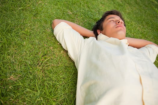 Man lying in grass with his eyes closed and his hands resting underneath his head