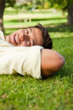 Man smiling while lying in grass with his hands resting underneath the side of his head