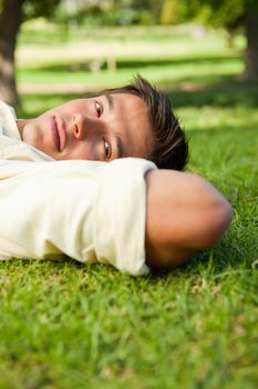 Man with serious expression lying in grass with his hands resting underneath the side of his head