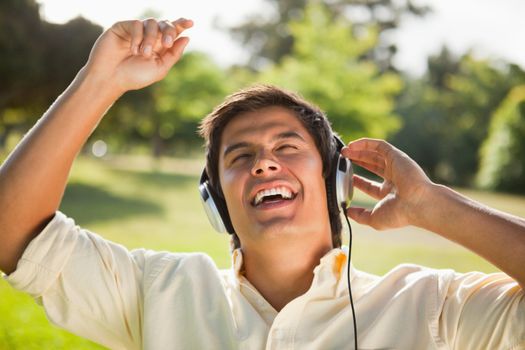 Man singing with his arms raised as he uses headphones to listen to music in a park