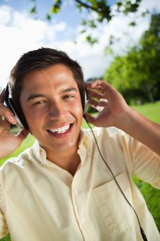 Man with a joyful expression while using headphones to listen to music in a park