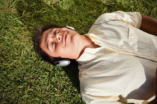 Man closes his eyes as he uses headphones to listen to music while he lies down on the grass