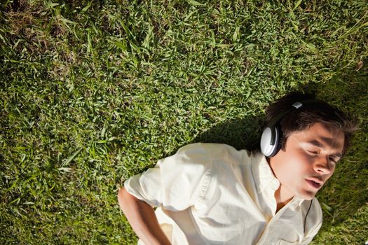 Elevated view of a man with his eyes closed while using headphones to listen to music as he lies down on the grass