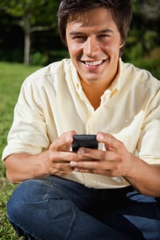 Man smiling while he sends a text message as he is sitting down on the grass