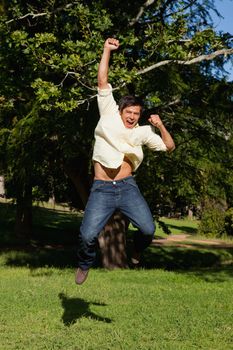 Man laughing as he jumps off the ground while raising his arms in celebration in the park