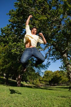 Man looks downwards as he jumps off the ground while raising his arms in celebration in the park