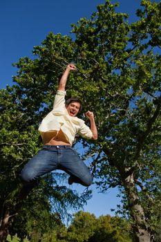 Man jumping off the ground while raising both his arms and his legs while he is celebrating in the park