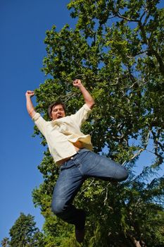 Man jumping off the ground while raising both of his arms and both of his legs while he is celebrating in the park