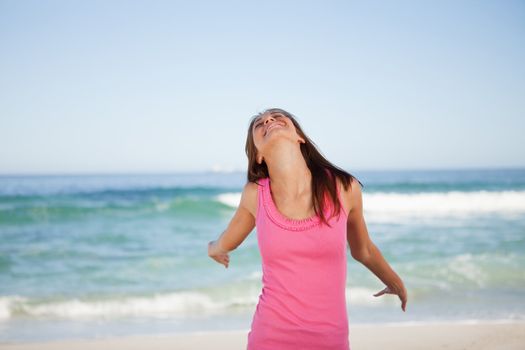 Young woman standing on the beach while enjoying the sun and beaming