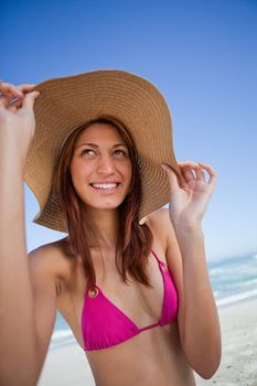 Smiling attractive teenager holding her hat brim while standing on the beach