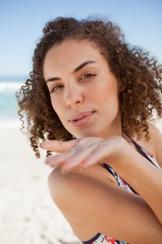 Young woman sending a kiss while gently blowing on her hand on the beach