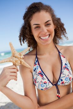 Smiling young woman holding a starfish while standing on the beach