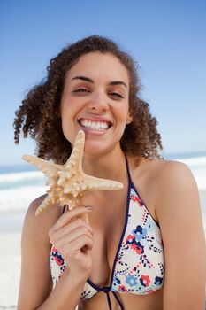 Smiling young attractive woman proudly holding a starfish on the beach