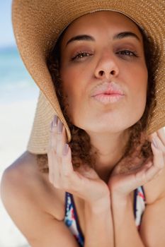 Young woman wearing a straw hat while puckering her lips in front of the sea