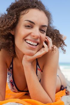 Smiling attractive woman lying on the beach with her hand on her cheek 