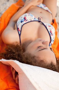Young relaxed woman napping on her beach towel while sunbathing