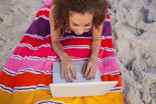 Overhead view of a young woman using her laptop while lying on the beach