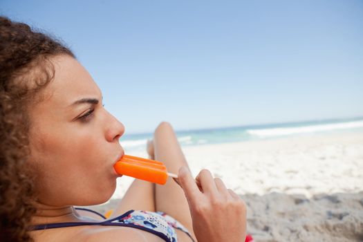 Young attractive woman eating a popsicle while lying on her beach towel