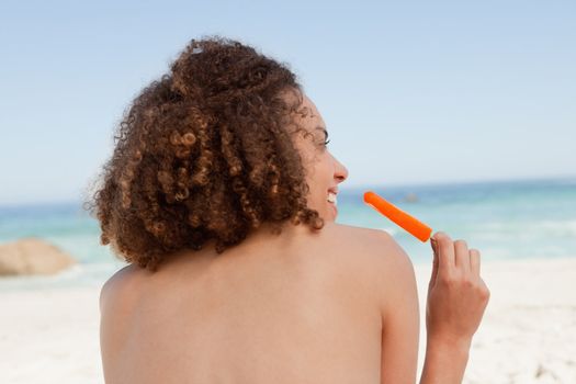 Smiling attractive woman holding an orange ice lolly in front of the ocean