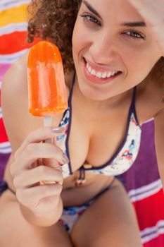 Young smiling woman holding a delicious ice lolly while sitting on a beach towel