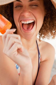 Young beautiful woman laughing and sitting on the beach while holding an ice cream