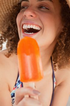 Laughing young woman looking towards the side while holding an orange popsicle
