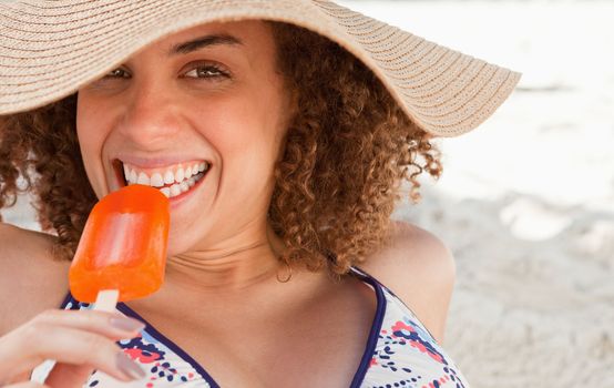 Young woman looking at the camera while eating a delicious ice cream on the beach
