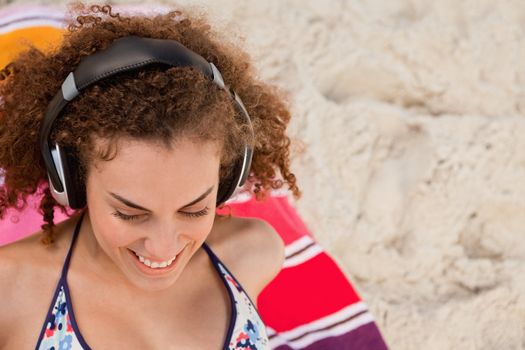 Smiling young woman listening to music with her headset while sitting on her towel