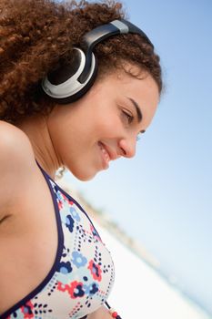 Beautiful young woman in swimsuit listening to music with a headset on the beach