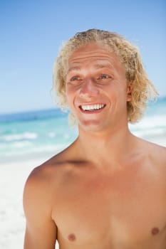 Surprised young blonde man looking towards the side while standing on the beach