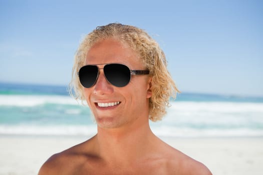 Smiling blonde man wearing sunglasses while standing in front of the ocean