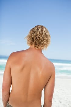Rear view of a young blonde man looking at the ocean while standing on the beach