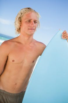 Young attractive man holding his perched surfboard while standing on the beach