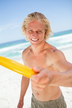 Smiling man holding a yellow frisbee while standing on the beach