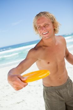 Smiling blonde man standing upright while holding a yellow frisbee