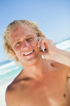 Smiling blonde man looking at the camera while talking on his mobile phone