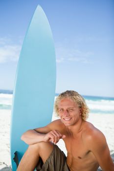 Blond man sitting in front of the ocean with his arm on his leg 