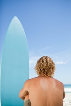 Rear view of a blonde man waiting for a wave while sitting next to his surfboard