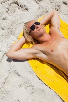 Overhead view of a blonde man lying on his beach towel while wearing sunglasses