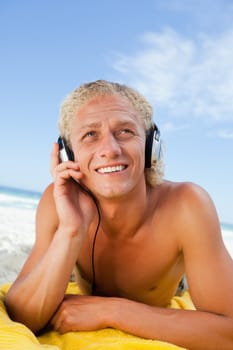 Smiling man lying on his beach towel while listening to music with his headset