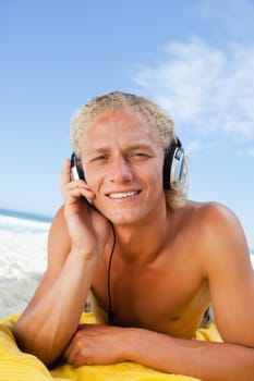 Young blonde man attentively listening to music while lying on then beach