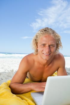 Smiling blonde man looking at the camera while lying down behind his laptop