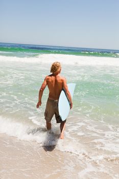 Young blonde man holding his blue surfboard while starting to walk in the water