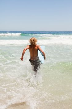 Young blonde man holding his blue surfboard while wading in the water