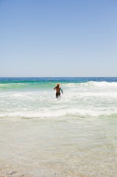 Rear view of a blonde man running fast in the water while holding his blue surfboard