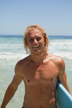 Smiling blonde man standing in the water with his blue surfboard