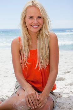 Young blonde woman sitting on the beach while showing a great smile