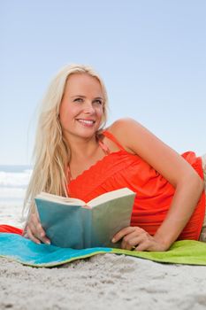 Young smiling blonde woman looking up while lying on her side and reading a book